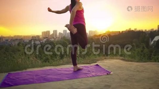 一个年轻的女人在大城市的背景下在山上练习瑜伽。 健康的女人在日落时做运动。 A.视频