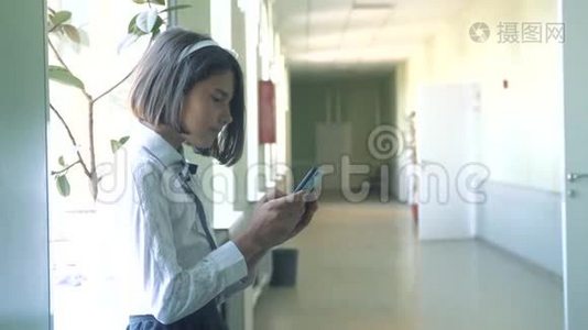 在学校概念上使用智能手机的女学生教育。 年轻的女孩，用智能手机站在窗户旁边视频