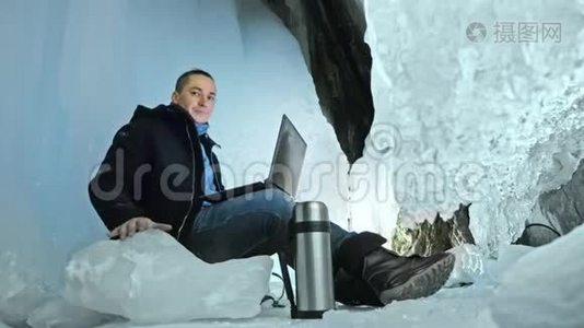 人们坐在冰洞里的笔记本电脑上。 围绕着神秘美丽的冰窟.. 用户在视频