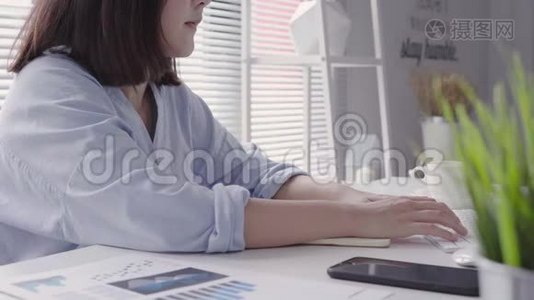 美丽的年轻微笑的亚洲女人，在家里坐在客厅里用笔记本电脑工作。视频