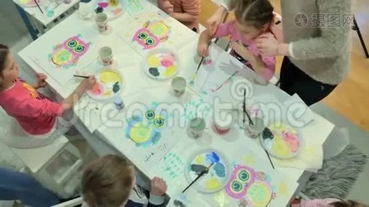 孩子们，男孩和女孩在教室里围着桌子坐在一起画画。 与他们在一起的是他们的年轻视频
