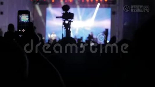音乐音乐会上的人群。 在明亮多彩的舞台灯光前，成群的观众在智能手机上拍照视频