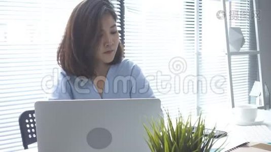 美丽的年轻微笑的亚洲女人，在家里坐在客厅里用笔记本电脑工作。视频