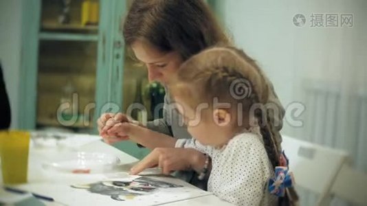 孩子们女孩坐在教室的桌子旁，用手指和油漆画画。 带着他们视频