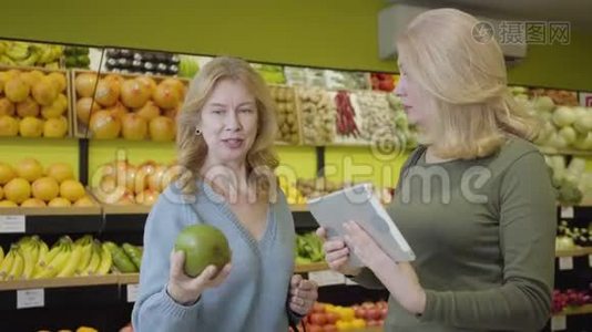 成年白种人女性使用平板电脑检查水果来源。 积极的家庭主妇在杂货店买柚子。 生活方式视频