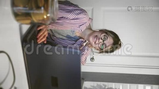 通过电话会议交流的年轻女性垂直视频，在厨房里用笔记本电脑看电脑。视频