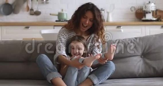 快乐的小妈妈和可爱的小女儿在沙发上玩耍视频