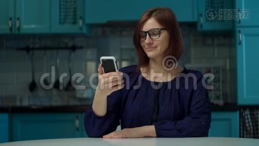 30多岁的年轻女性戴眼镜，在检疫期间通过手机应用程序在家厨房进行在线订购。 妇女收到视频