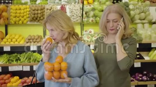 漂亮的高白种人女人闻着新鲜美味的橘子，就像她的女朋友在电话里说话一样。 积极正面视频