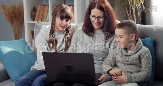 微笑的母亲和孩子们用笔记本电脑在沙发上放松视频