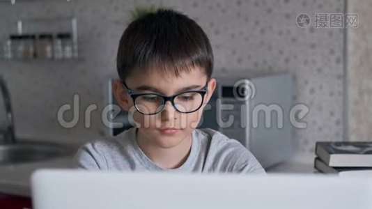 肖像。 小学生在餐桌旁的厨房里坐着，用笔记本电脑做作业。视频