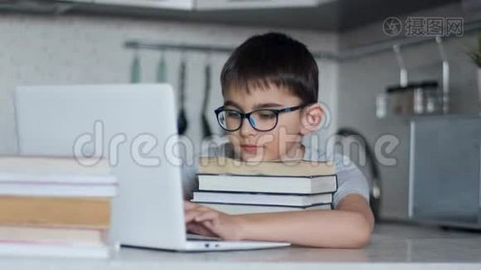 一个小学生在餐桌旁坐在厨房里做家庭作业，使用大量的教科书和笔记本电脑。 网上在线视频
