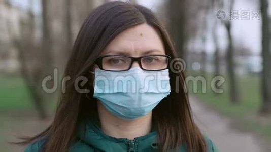 一个戴着眼镜和医用口罩的年轻女孩站在街上。视频