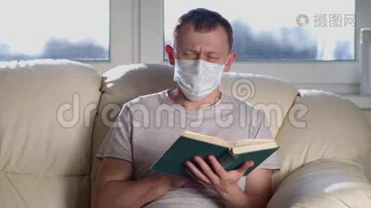 戴着医疗面具的男人手里拿着一本书坐在沙发上看着相机视频