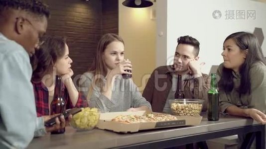 快乐的多民族朋友在家客厅喝啤酒，吃披萨，交流..视频