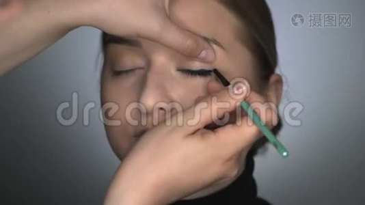 化妆师为美容工作室的年轻女性制作专业化妆。 化妆师将黑色眼线涂于视频