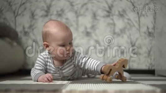 一个穿着条纹睡衣的金发小宝宝和一匹木马在地板上玩耍，试图吃掉它视频