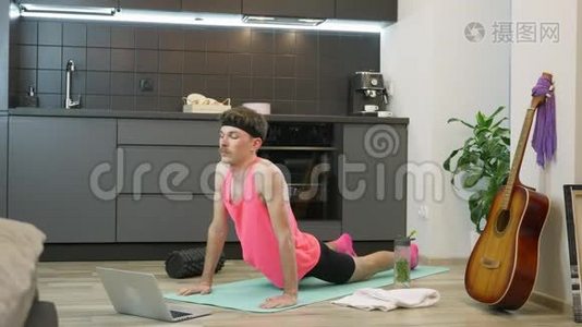 男人在厨房的家中在健身垫上做伸展运动。 粉色上衣练习伸展和瑜伽练习的搞笑男视频