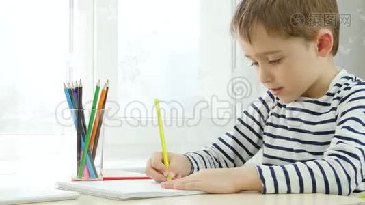 一个学龄前的男孩，用彩色铅笔画画，坐在桌子旁，坐在窗边。 体贴，聪明视频