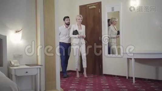 积极的高加索夫妇带着旅行袋进入酒店房间交谈。 抵达的满意酒店客人的肖像视频