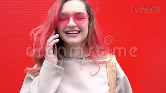 时尚肖像，美丽的微笑时髦女人戴太阳镜，红色头发与智能手机对抗。视频
