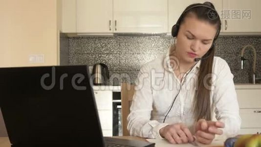 在家工作的年轻女人坐在厨房的桌子旁，看着笔记本电脑的屏幕，写下一些东西。 能力视频
