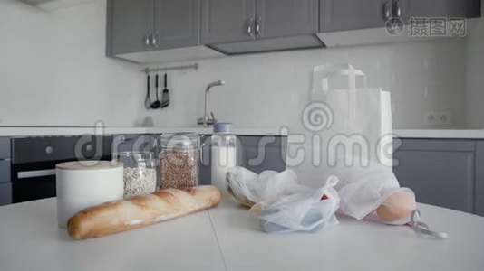厨房木制桌子上有面包、燕麦片、荞麦、牛奶、蔬菜和水果的未包装购物袋。 青年视频