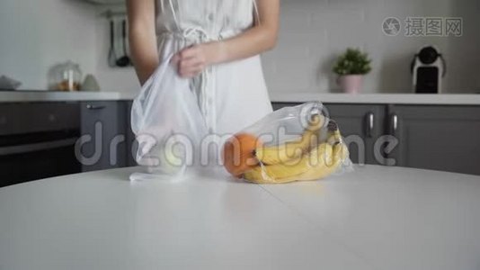 年轻的女人把水果从塑料袋移到厨房木桌上可重复使用的网袋。 零废物之家和生态袋视频