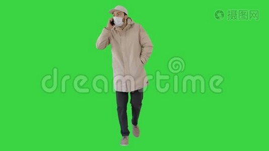 穿着户外衣服和医用面具的休闲男子在绿色屏幕上行走和在电话上交谈，Chroma键。视频