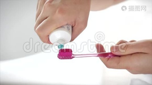 一只雌性的手把彩色牙膏挤到粉红色牙刷上。 现代浴室的口腔卫生。 特写镜头。视频
