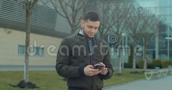 带着智能手机走在现代办公中心附近的男子肖像。在社交网络上和朋友聊天。看视频
