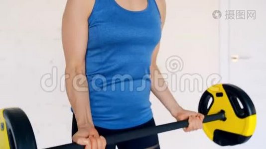 穿运动服的强壮漂亮的女孩用杠铃做二头肌运动。 她在家里的客厅里接受训练视频