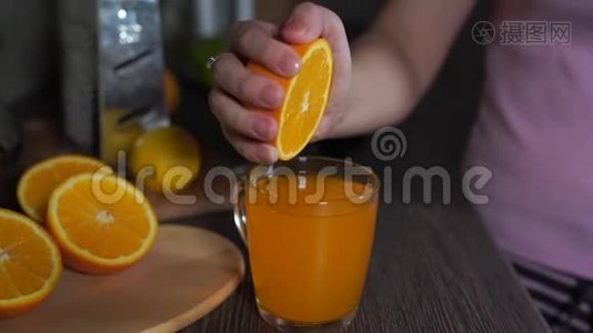 一个女孩在厨房里挤压一个橘子，得到新鲜的橙汁，特写。 女人挤橙汁视频