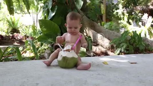 快乐的宝宝坐在街上的地上，玩着新鲜的绿椰子。视频
