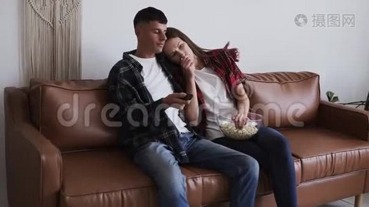 敏感的女人在看电视和哭泣，而丈夫在家。 一对夫妇坐在棕色的皮椅上，丈夫视频