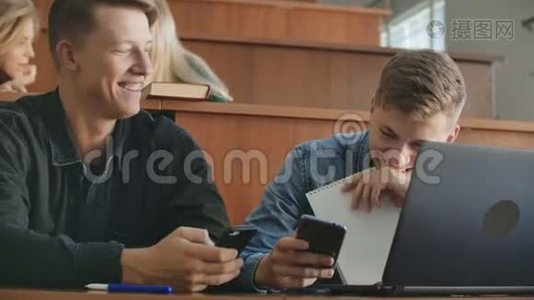 在大学演讲的休息时间，手持智能手机的男生在观众中大笑视频