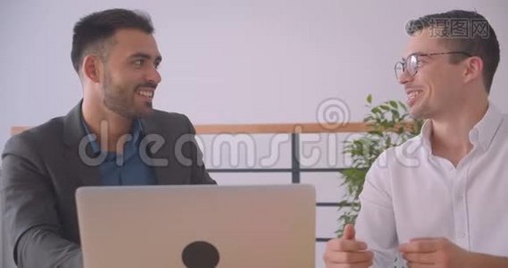 两位有魅力的商人在办公室室内一起讨论笔记本电脑项目的特写照片视频