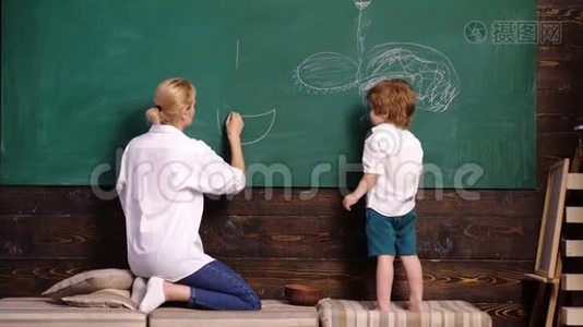 幼儿教师和幼儿男孩在黑板上作画。 女人和男孩画画。 母亲和儿子用粉笔在视频