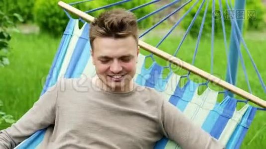 一个快乐男人的特写肖像躺在花园的吊床上，微笑着放松视频