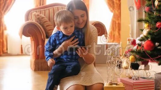圣诞节早上在客厅里，小男孩和妈妈在智能手机上看动画片的4k视频。 家庭成员视频