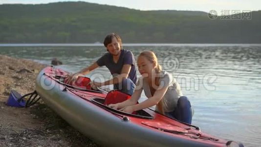 年轻的男人和女人准备他们的充气皮艇在湖或海中划水。 慢镜头视频