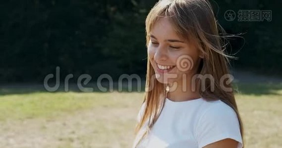 年轻迷人的女性的肖像，她微笑着看着绿色草坪上的相机。 快乐的年轻女孩。 关门视频
