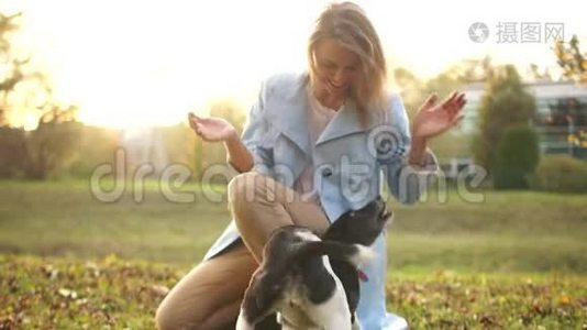 可爱的穿着蓝色斗篷的年轻女人正在公园里和她的黑白狗玩。 秋天和宠物散步视频