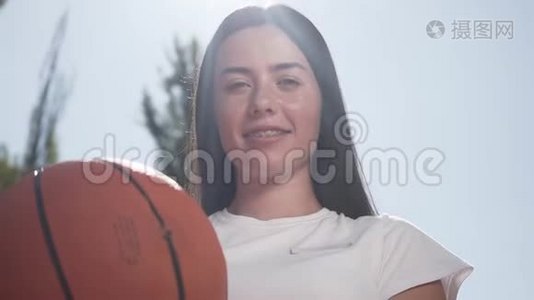 一幅美丽的黑发女人的肖像，戴着牙套，拿着篮球，看着镜头微笑。 概念视频