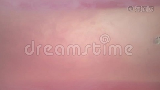 一种漂亮的丙烯酸墨水在水中的混合物。 混合时，白色和粉红色的墨水形成抽象的云。 丙烯酸视频