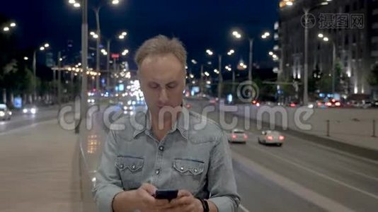 中年男子在晚间城市的女儿墙上使用智能手机视频