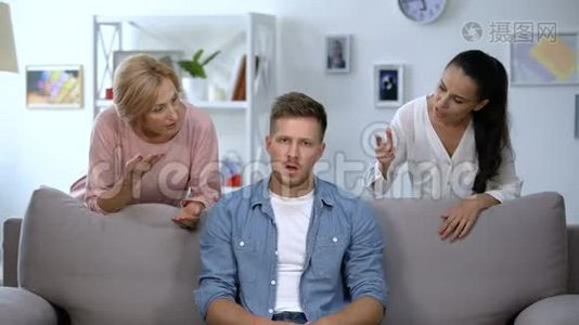 愤怒的男人坐在沙发上，倾听妻子和母亲的责备，问题视频