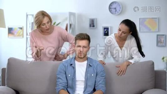 疲惫的男人坐在沙发上，忍受着妻子和母亲的批评，争吵视频
