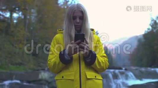 美丽迷人的白种人欧洲女孩使用她的智能手机在瀑布附近的山脉自然技术美丽视频