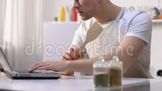 饥肠辘辘的男人在笔记本电脑上看菜谱，做业余搅拌配料视频